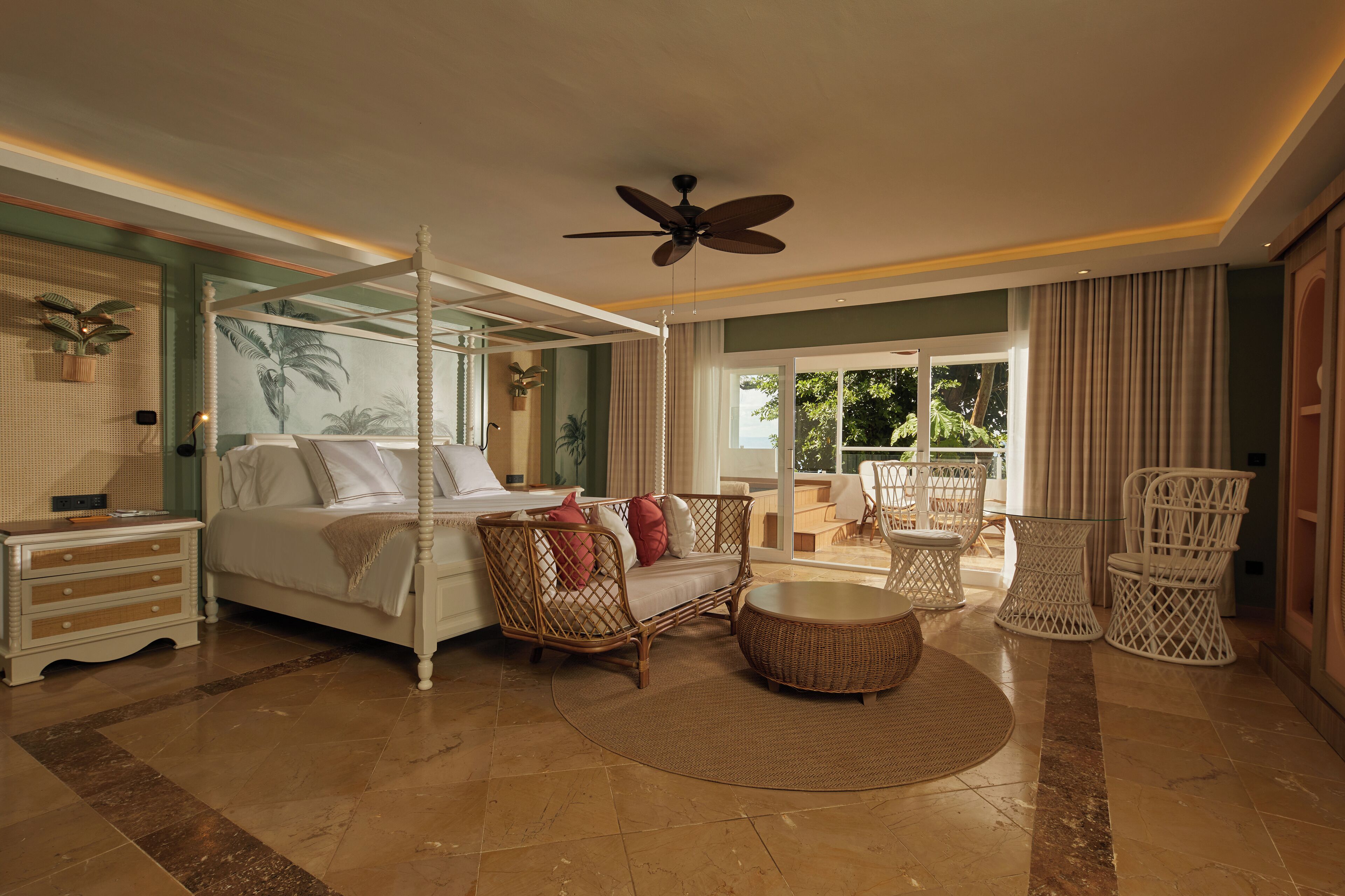A spacious bedroom with a four-poster bed, a ceiling fan, and a balcony with wicker furniture.