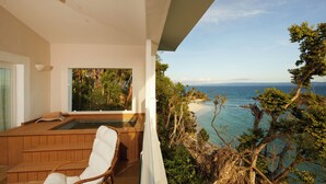 Un balcone con una sedia di legno, un tavolino e vista sulla spiaggia e sull'oceano.