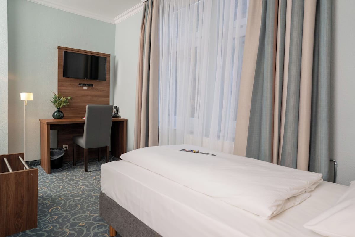 Una habitación de hotel con cama, escritorio y silla, televisor y ventana con cortinas.