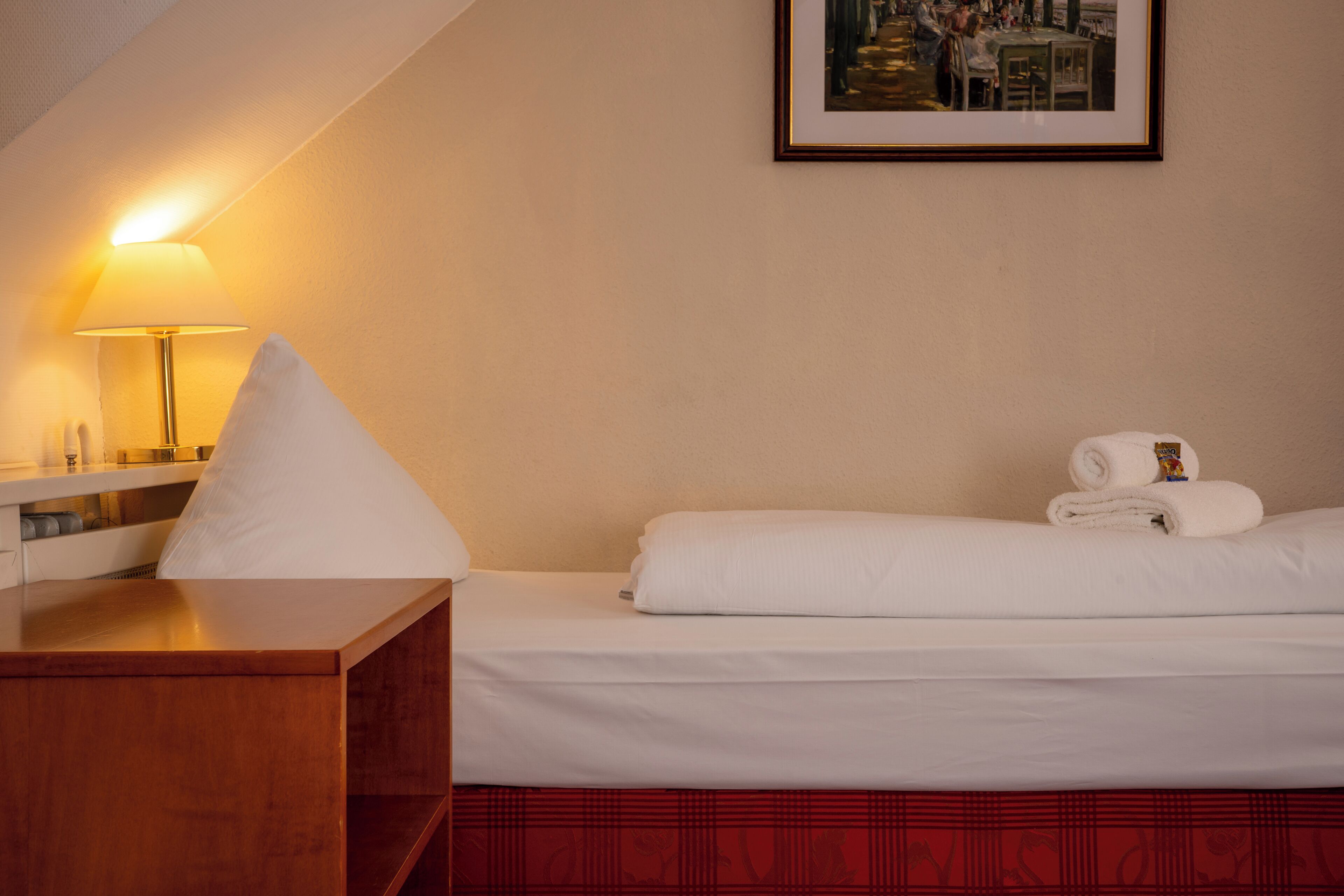 Une chambre d’hôtel avec un lit, une table de chevet, une lampe et un tableau encadré au mur.