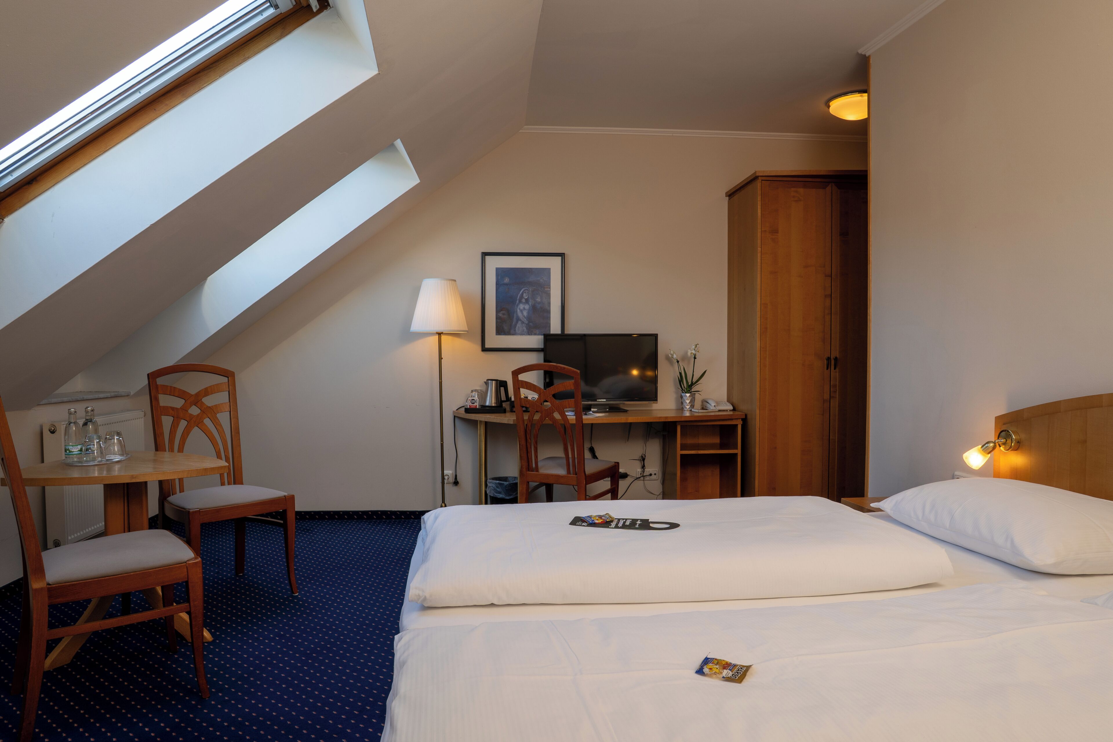 Una habitación de hotel con cama, escritorio con silla, televisión, lámpara y armario de madera.