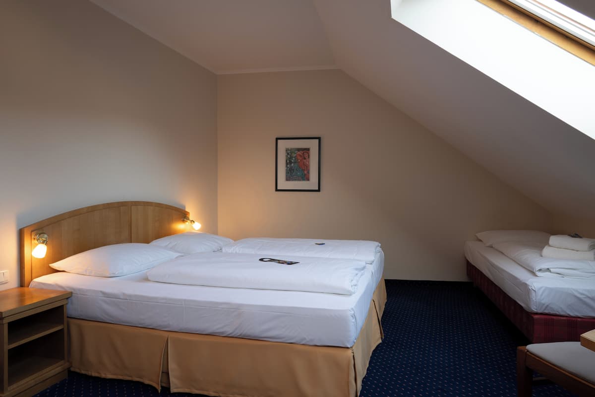 Habitación de hotel con una cama individual, una mesita de noche, una lámpara y un cuadro en la pared, además de un ventanal que proporciona luz natural.