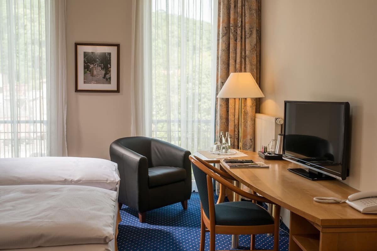 Una habitación de hotel con una cama, un escritorio con televisor, una silla y una lámpara.