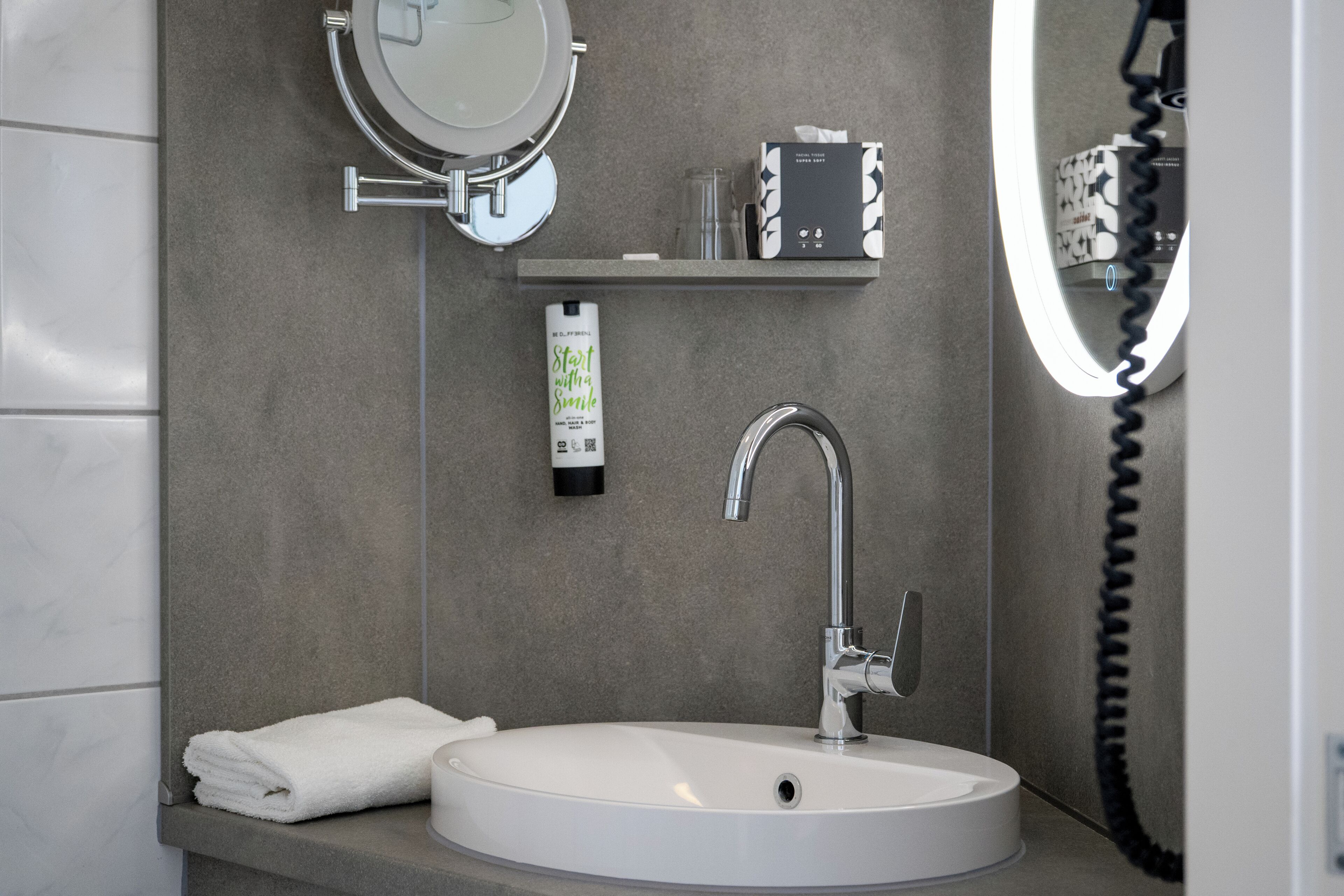 A bathroom with a white sink, a mirror, a towel, a soap dispenser, and a small shelf with toiletries.
