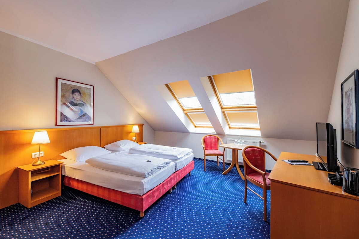 Habitación de hotel con cama, escritorio, silla, televisor y un cuadro en la pared.