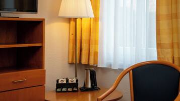 A room with a TV, a lamp, a coffee maker, and a chair.