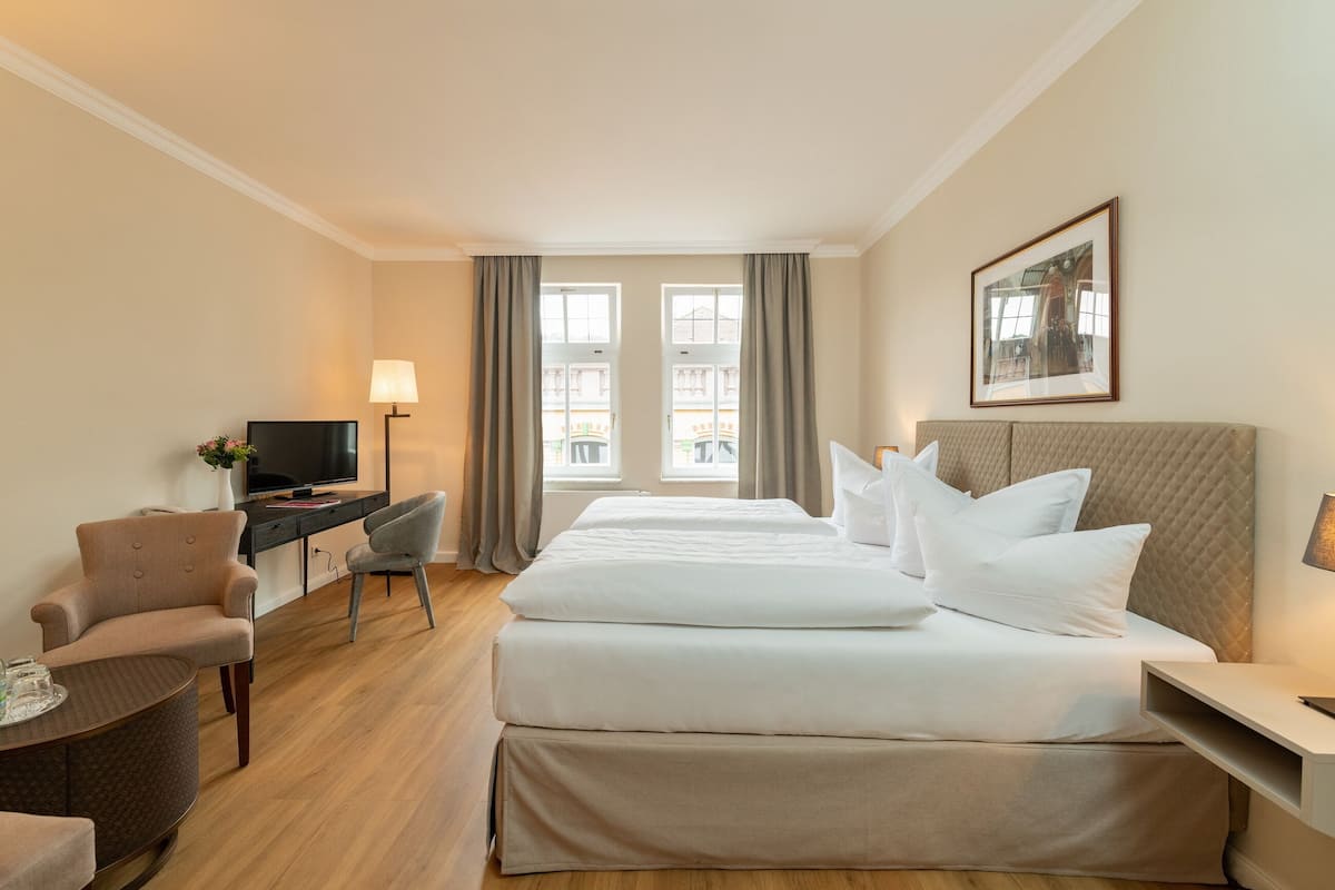 Habitación de hotel con cama, escritorio, silla, televisor y ventana con cortinas.