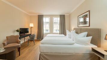 Habitación de hotel con cama, escritorio, silla, televisor y ventana con cortinas.