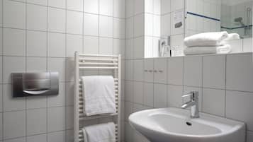 Ein Badezimmer mit weißen Fliesen, einem weißen Waschbecken, einem Handtuchhalter und einer Toilette.