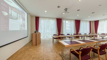 Una sala conferenze con un grande schermo che mostra informazioni sull'hotel, tavoli in legno, sedie rosse e un podio.