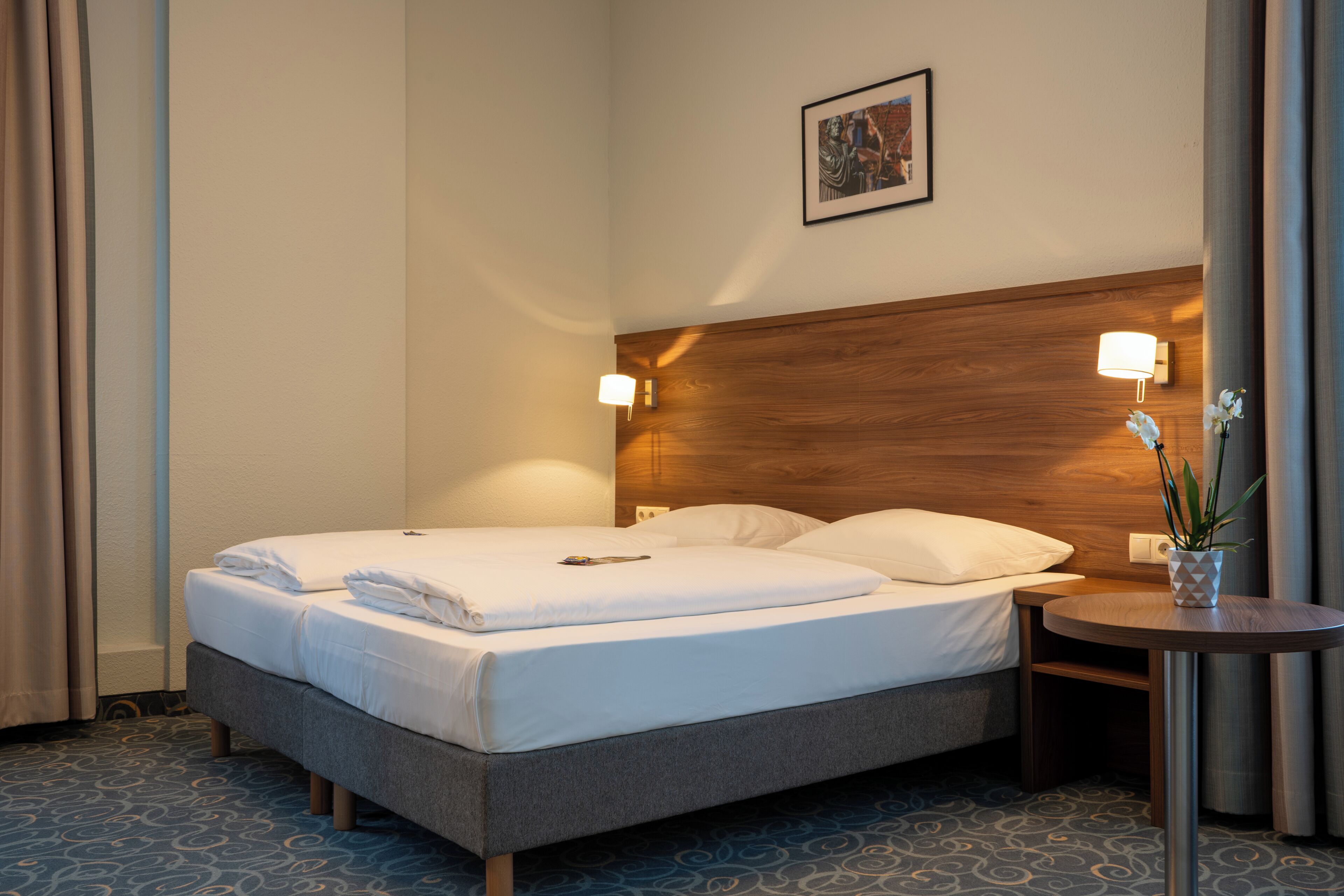 Ein Hotelzimmer mit einem Bett, Nachttischlampen, einem kleinen Tisch und einer Topfpflanze.