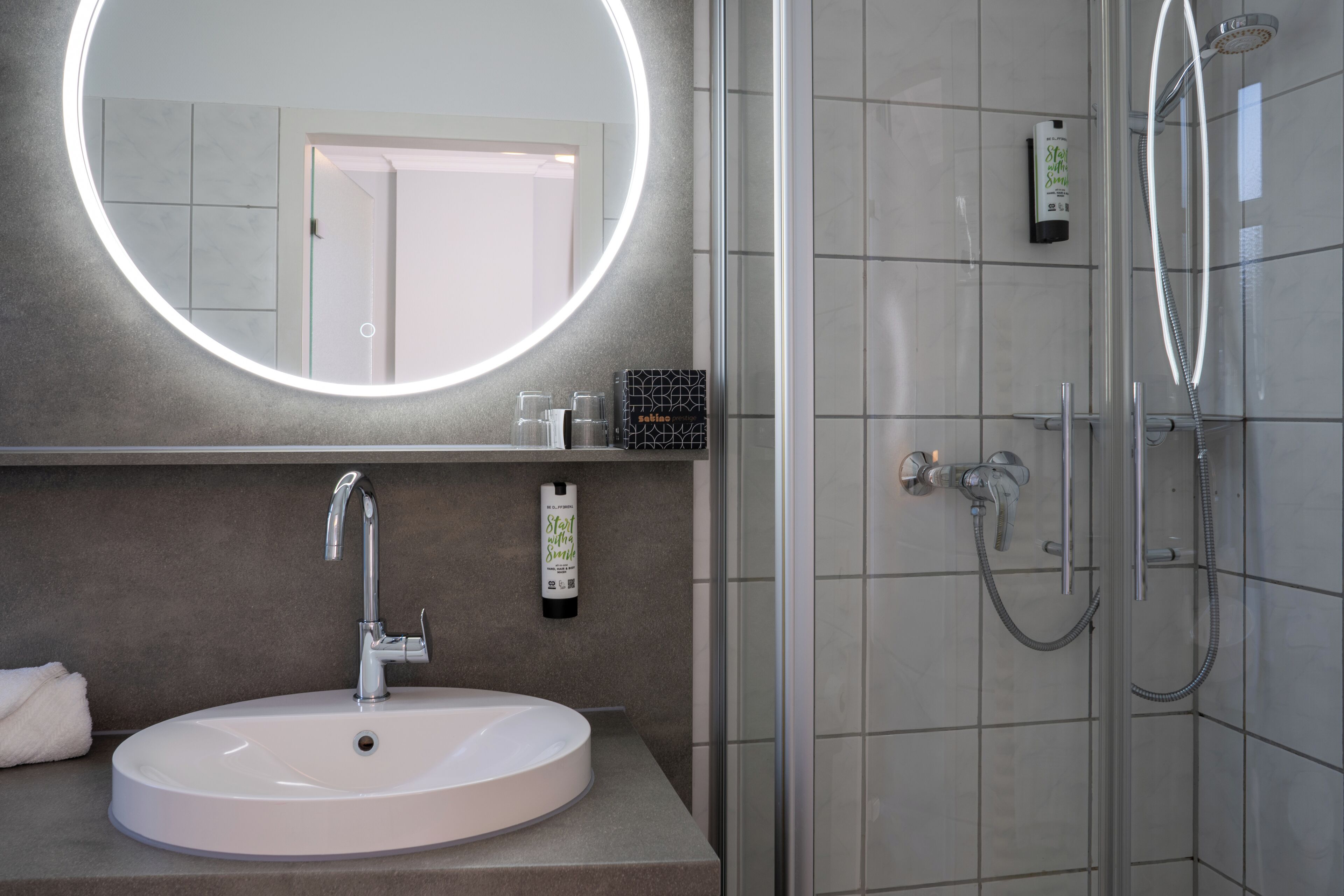 Ein Badezimmer mit rundem Spiegel, Waschbecken, Dusche und Handtuchhalter.