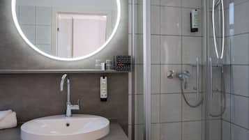 Ein Badezimmer mit rundem Spiegel, Waschbecken, Dusche und Handtuchhalter.