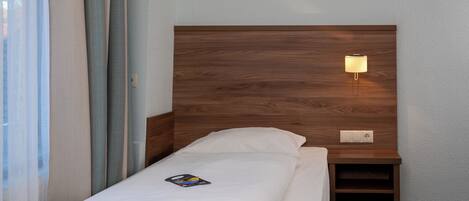 Una cama bien hecha con un cojín, una mesita de noche con una lámpara y un cuadro enmarcado en la pared.