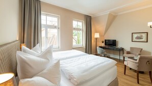 A hotel room with a large bed, a desk with a TV, a chair, and a lamp.