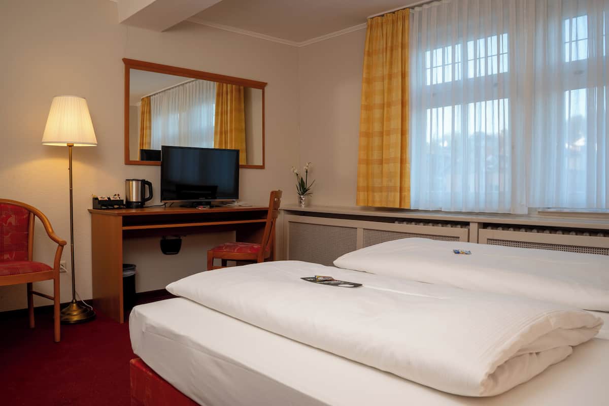 Habitación de hotel con cama, escritorio con televisor, silla y ventana con cortinas.