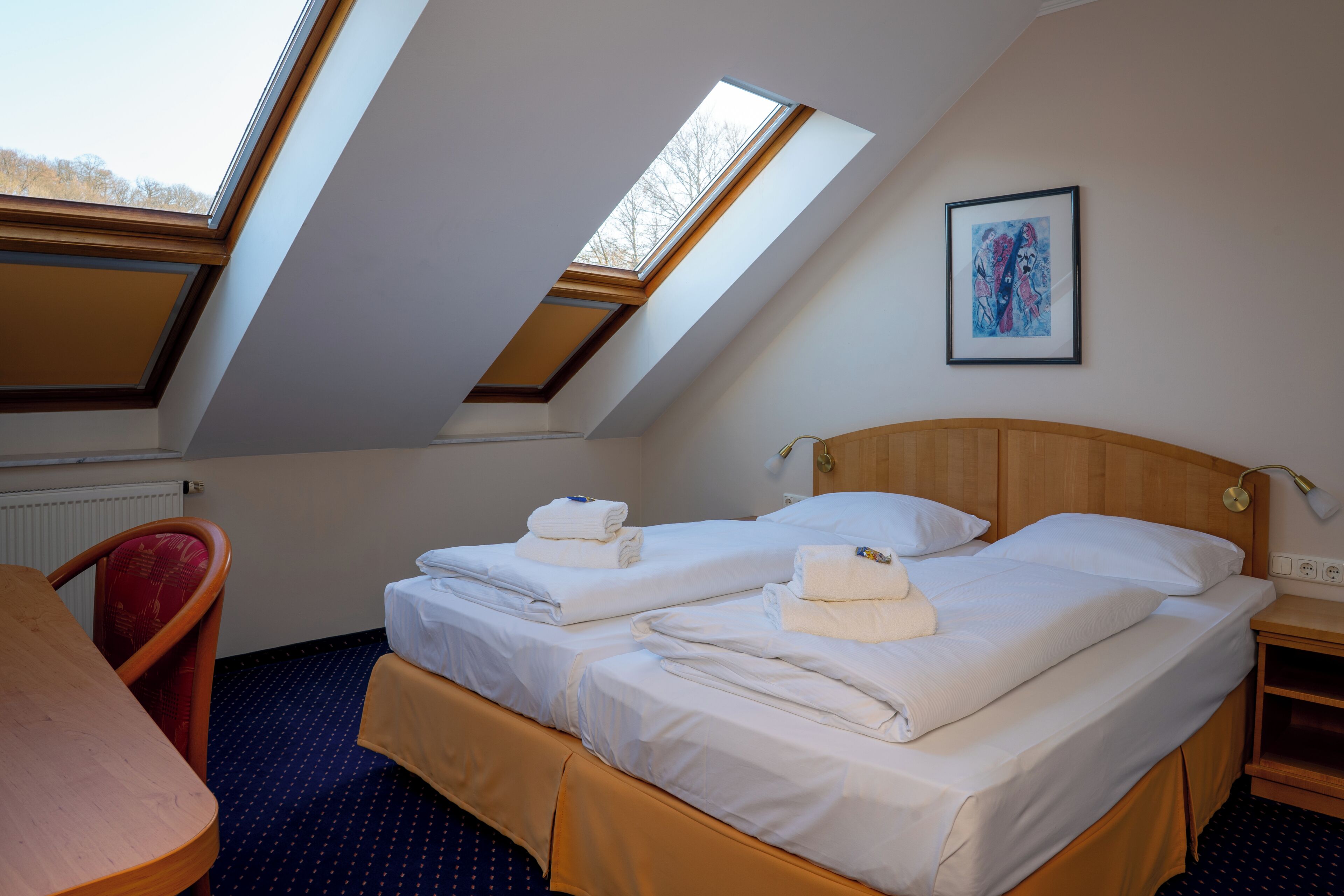Een hotelkamer met twee bedden, een eettafel, een stoel en een dakraam.