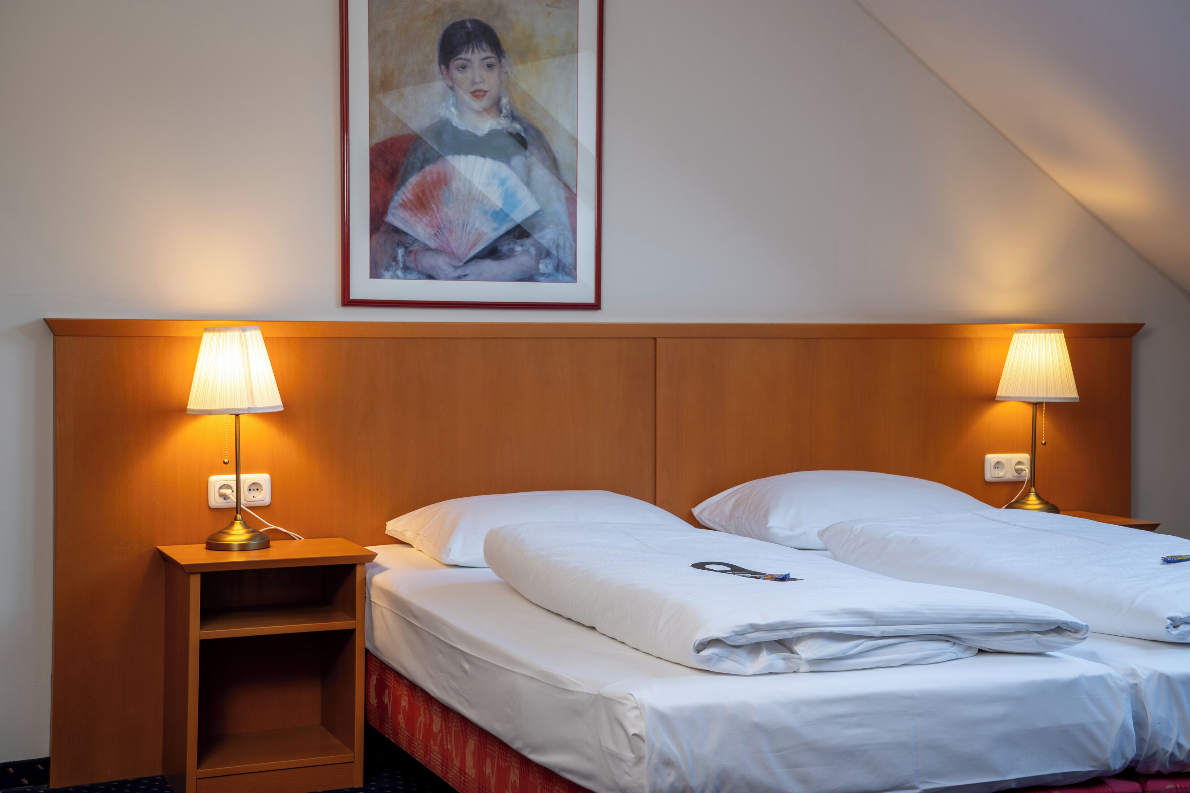 Une chambre d’hôtel avec deux lits, une tête de lit en bois, des lampes de chevet, un tableau au mur et une petite table de chevet en bois.