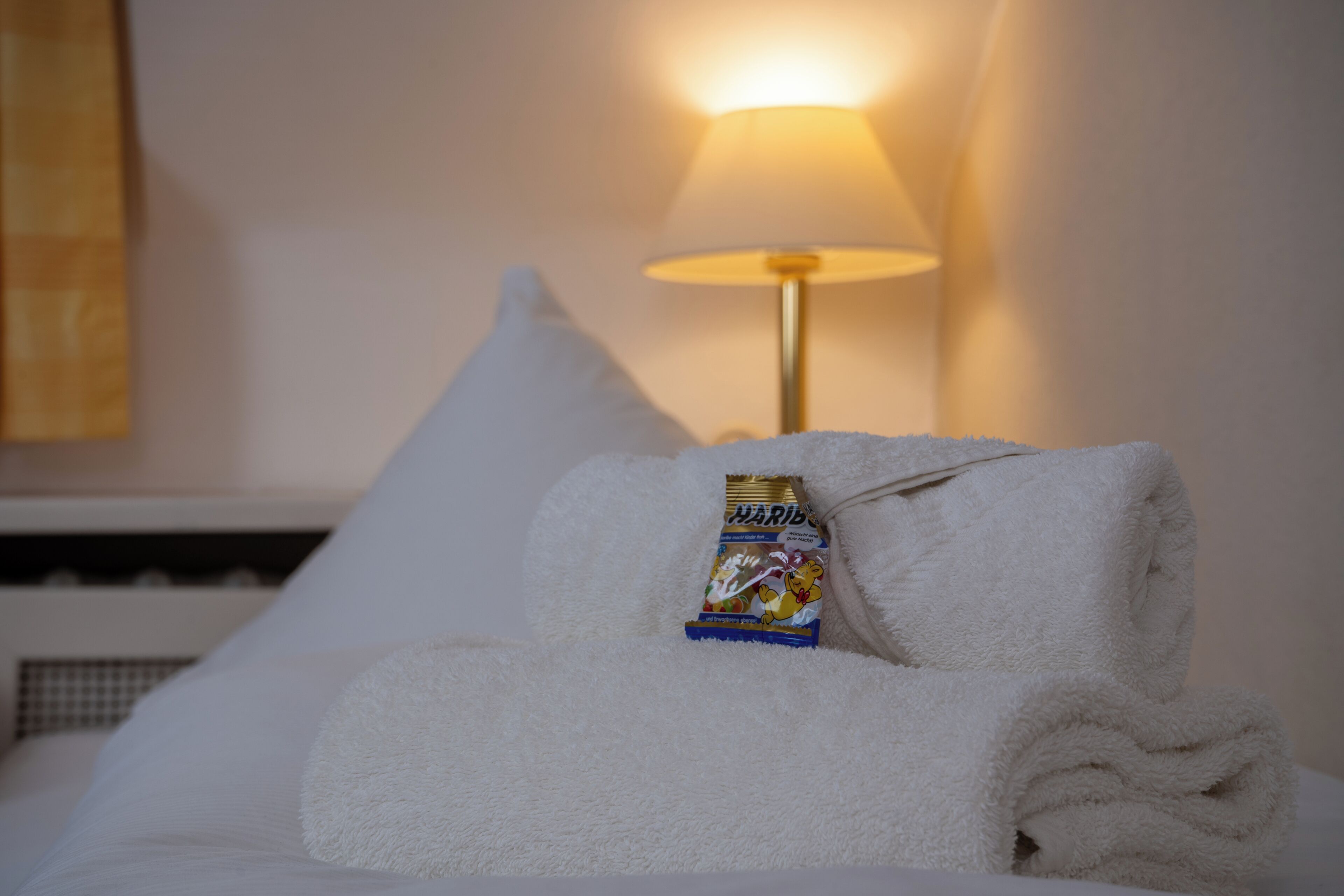 Una cama bien hecha con una toalla blanca doblada y una barra de caramelo Haribo.