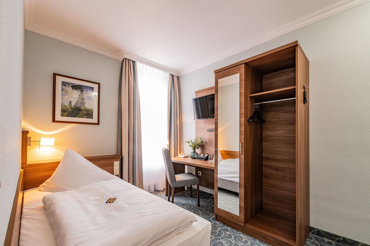 Una habitación de hotel con cama, escritorio, silla y armario.