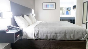 A neatly made bed with white bedding, a bedside phone, and a small table with a book and a pen. - Quality Inn Carrollton Medical Center (Carrollton)