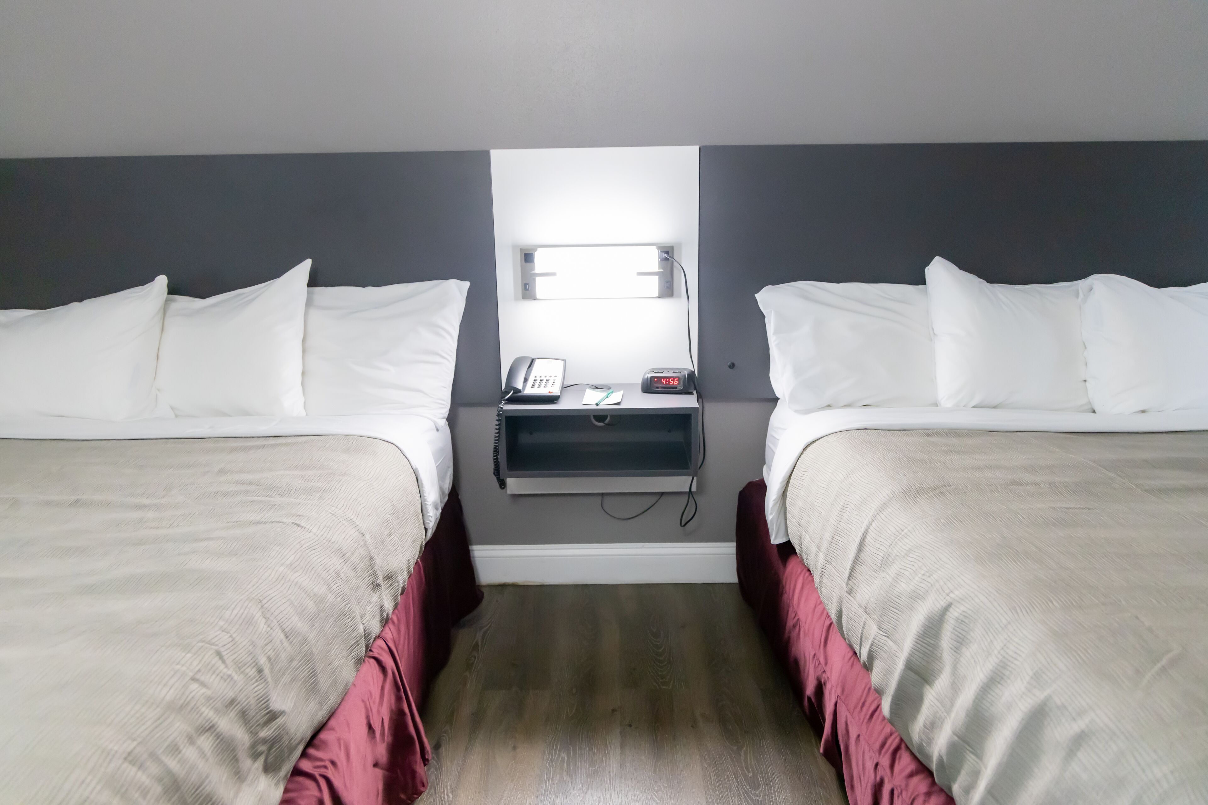 Habitación de hotel con dos camas, una mesita de noche con teléfono y reloj, y una pequeña estantería.