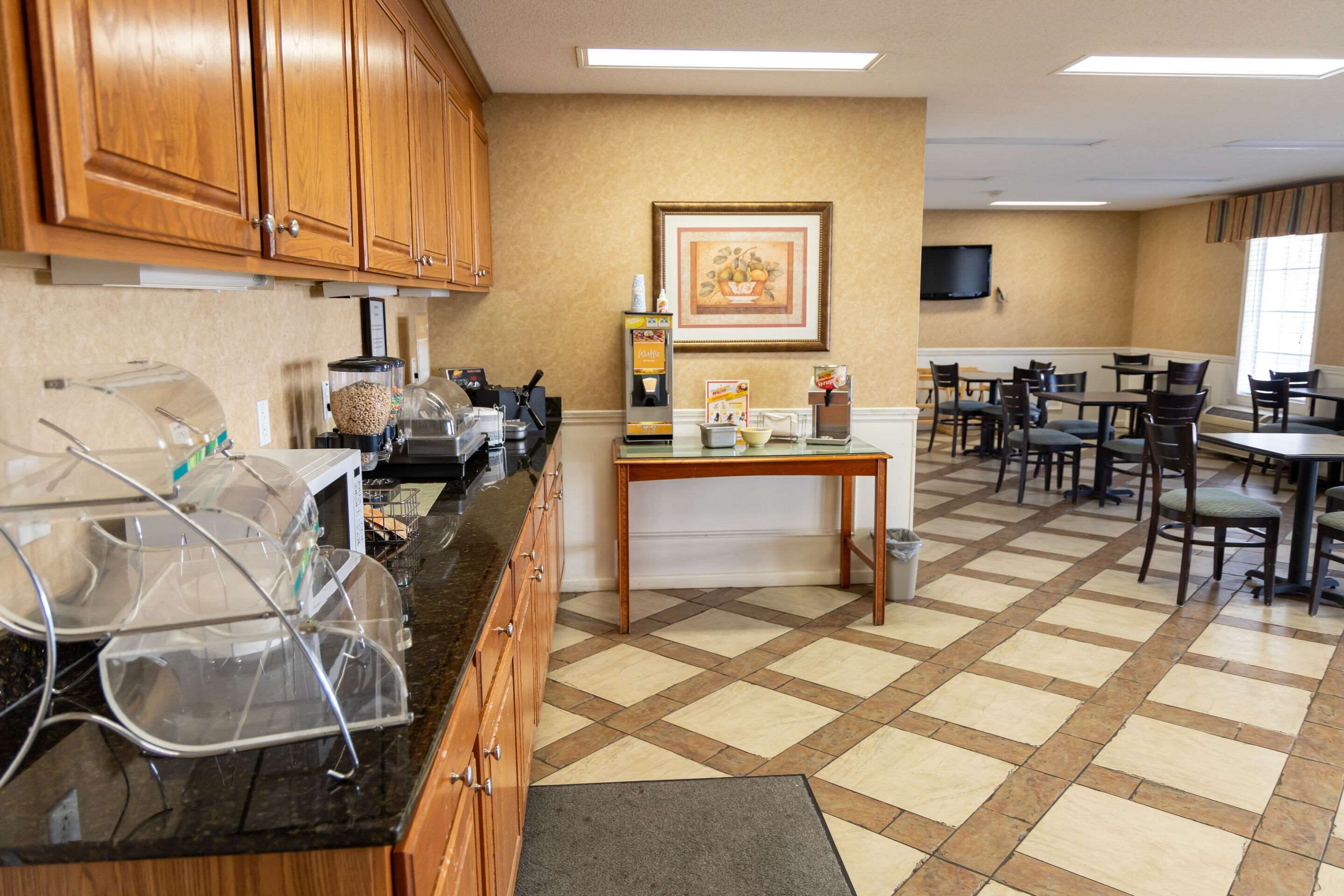 Una cocina de hotel con armarios de madera, una máquina de café y una zona de bufé con mesas y sillas.