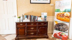 A reception area with a wooden desk, a framed picture on the wall, and a poster advertising breakfast. - Quality Inn Carrollton Medical Center (Carrollton)