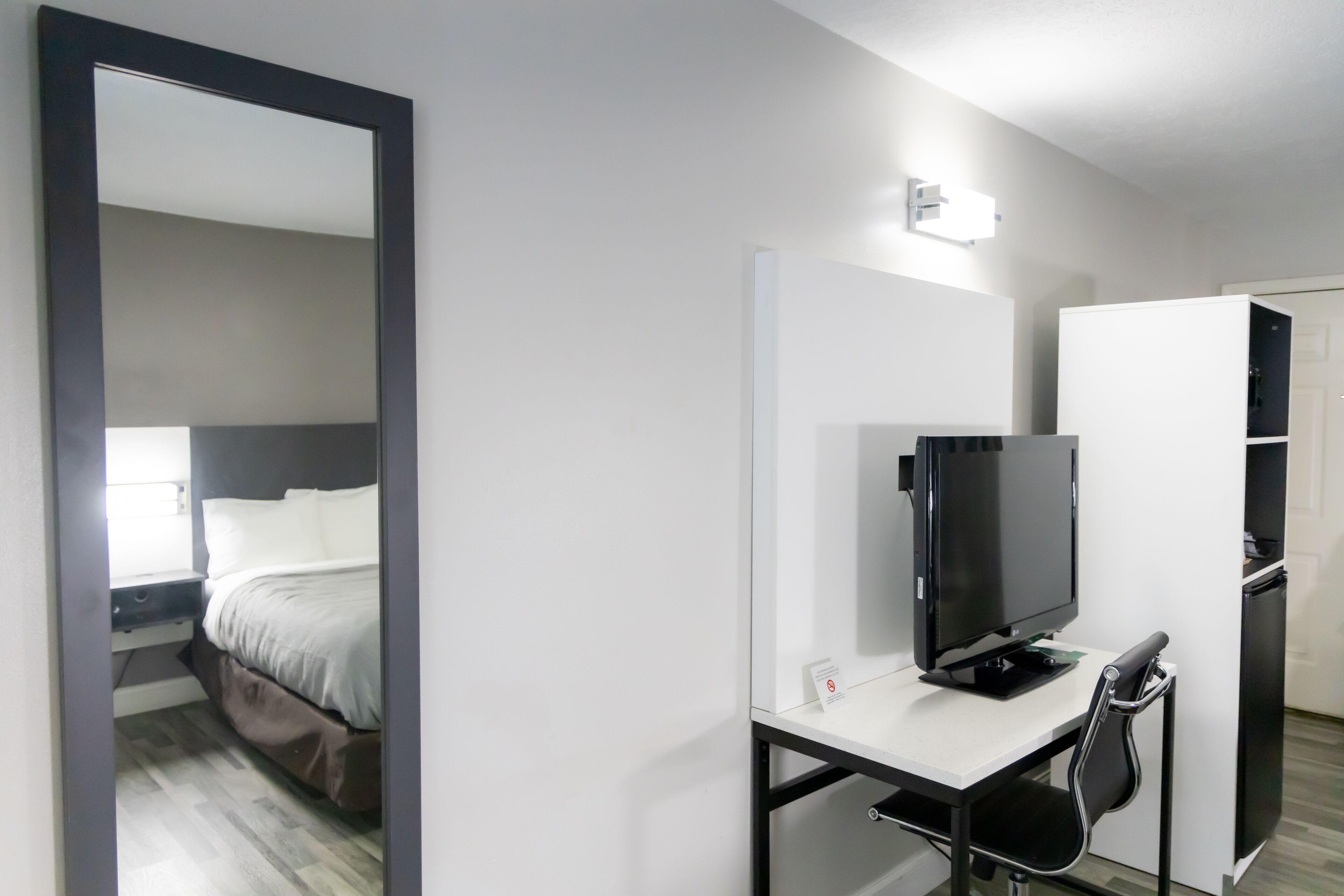 A hotel room with a bed, a desk with a computer and chair, a TV, and a wardrobe.