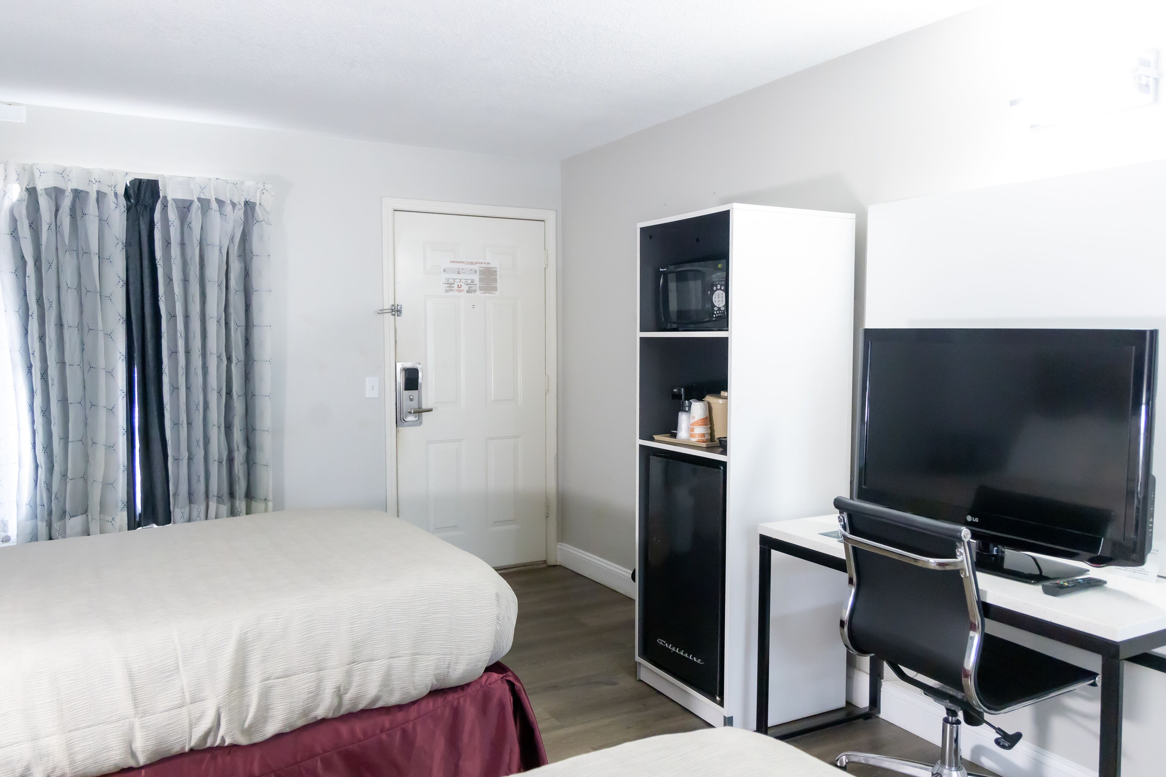 A hotel room with a bed, a desk with a computer and a TV, a microwave, and a small cabinet.