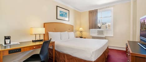 Habitación de hotel con cama, escritorio, silla y ventana con vista a la ciudad.