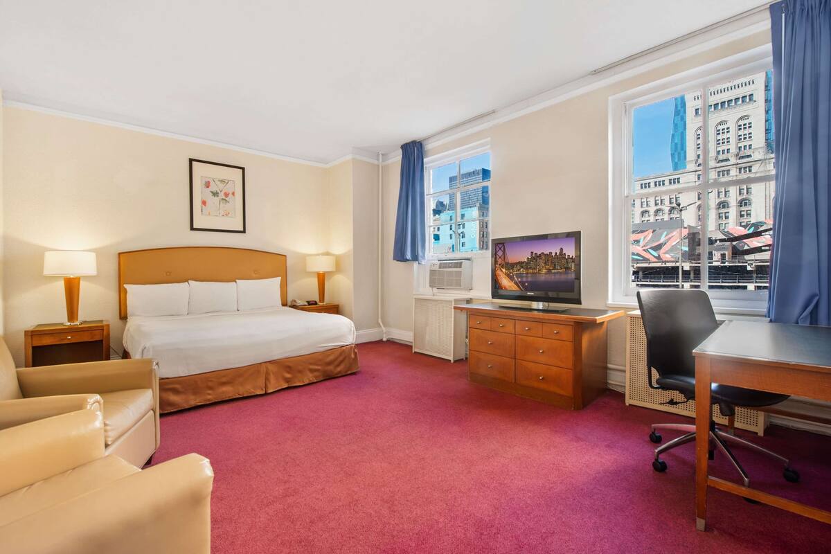 A hotel room with a bed, desk, chair, and a television.