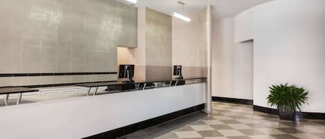 A modern hotel lobby with a check-in counter, a large mirror, and a potted plant.