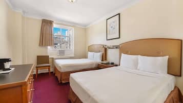 Habitación de hotel con dos camas, un escritorio, una silla, un ventanal con vista a edificios y un cuadro en la pared.