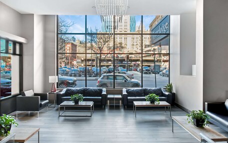 A modern hotel lobby with large windows, leather sofas, and a view of the cityscape.
