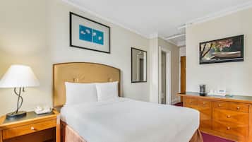 Una habitación de hotel con cama, mesita de noche, lámpara, cómoda y obras de arte en las paredes.