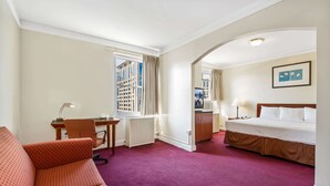 A hotel room with a bed, a desk with a chair, a sofa, and a view of a building through the window. - Travelodge by Wyndham Downtown Chicago (Chicago)