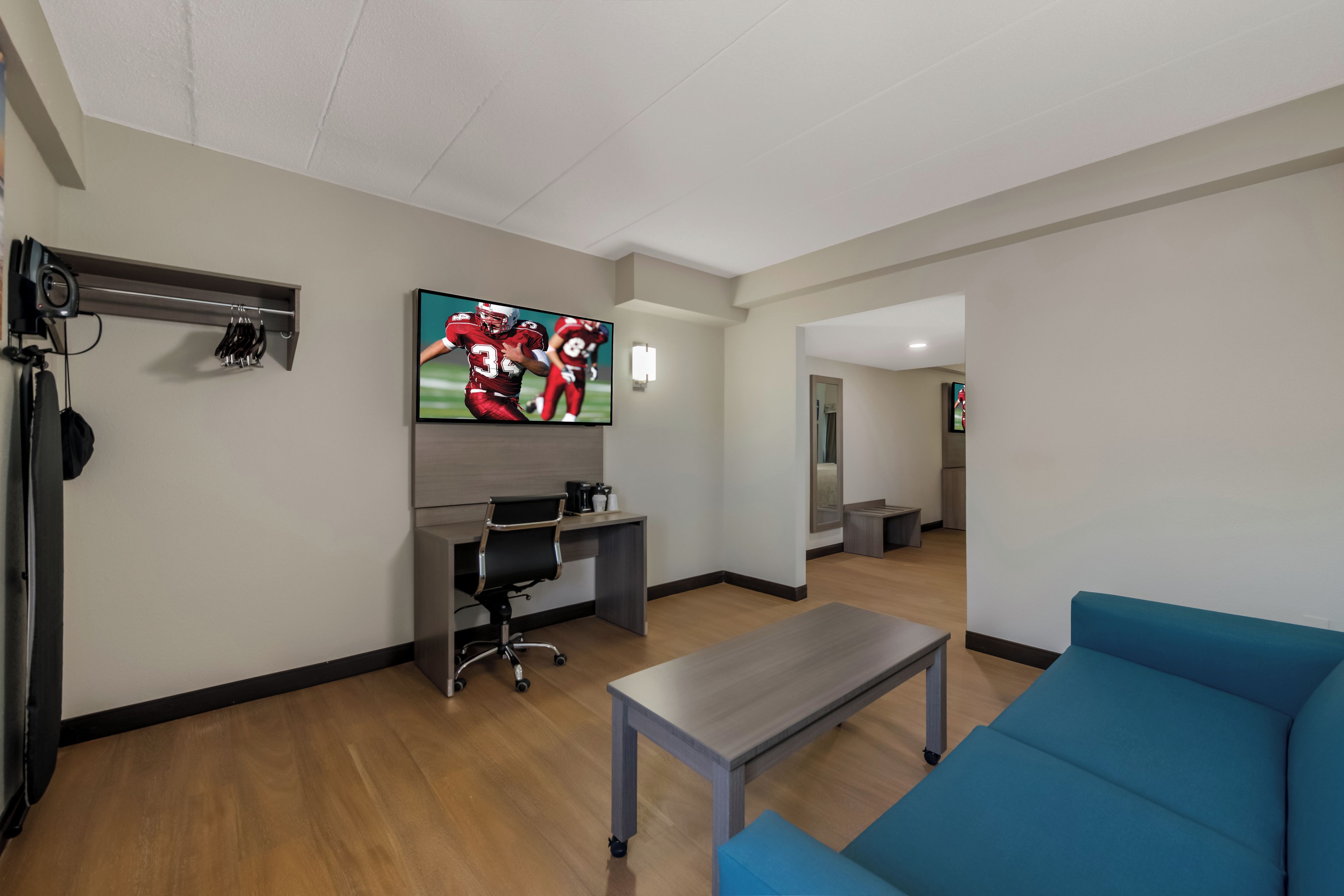 A modern living room with a flat-screen TV, a desk, a blue sofa, and a coffee table.