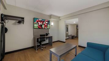 A modern living room with a flat-screen TV, a desk, a blue sofa, and a coffee table.