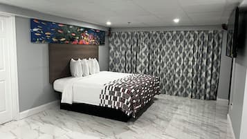 A bedroom with a bed, a headboard, a wall-mounted artwork, patterned curtains, and a tiled floor.