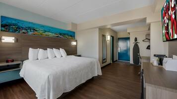 A hotel room with a bed, a painting of an underwater scene, a desk with a computer, and a door leading to another room.