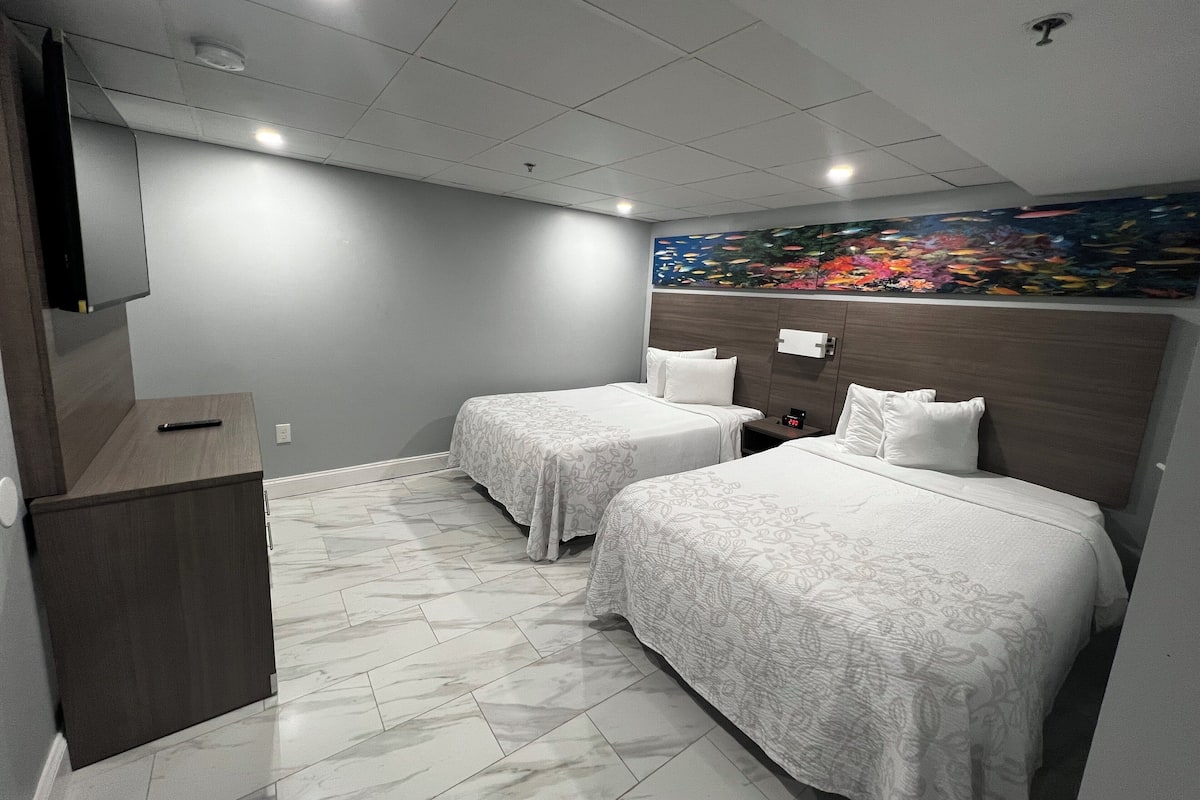 Habitación de hotel con dos camas, piso de mármol, un cuadro en la pared y un televisor montado en la pared.