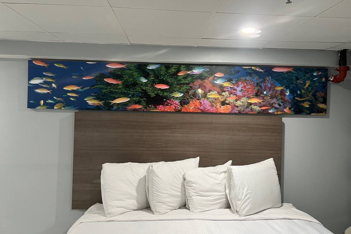 Un dormitorio con cama, almohadas blancas y un mural grande con una escena submarina.