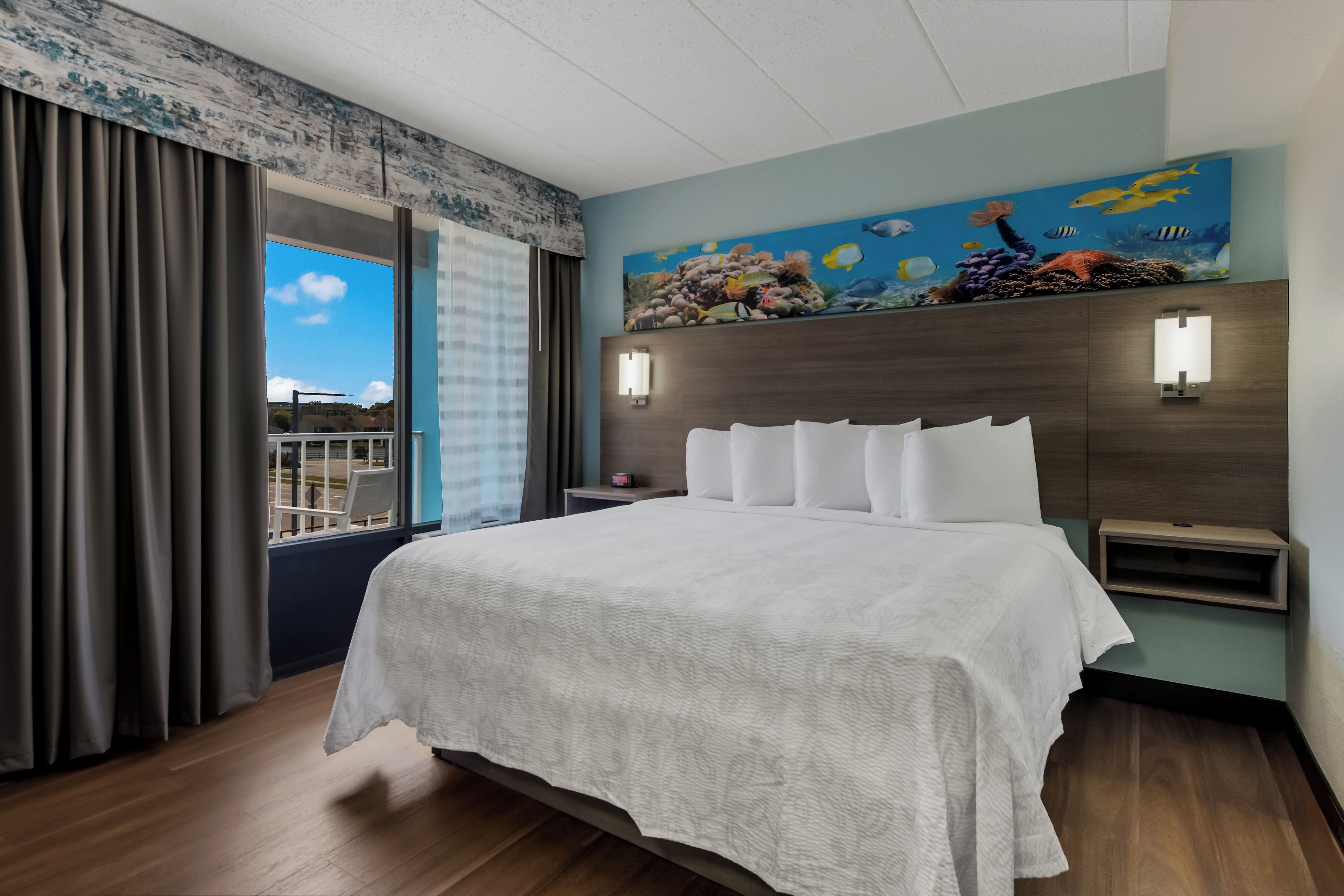 A hotel room with a large bed, a view of the outdoors through a window, and a mural of marine life on the wall.