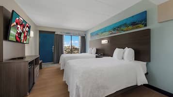 Habitación de hotel con dos camas, televisión, un cuadro y vista a la ciudad.
