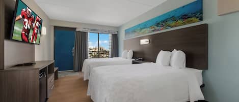 A hotel room with two beds, a TV, a painting, and a view of the city.