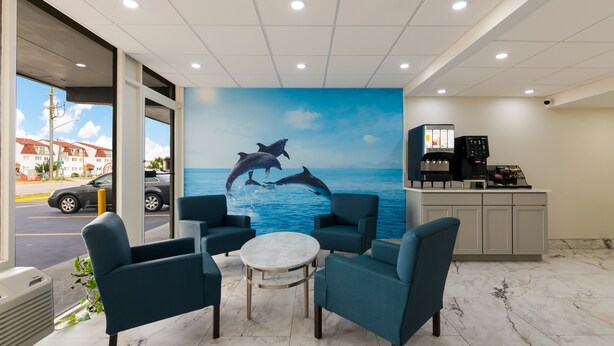 A lobby with teal chairs, a marble floor, a coffee machine, and a mural of dolphins jumping out of the water. - Red Roof Inn PLUS+ & Suites Virginia Beach – Seaside (Virginia Beach)