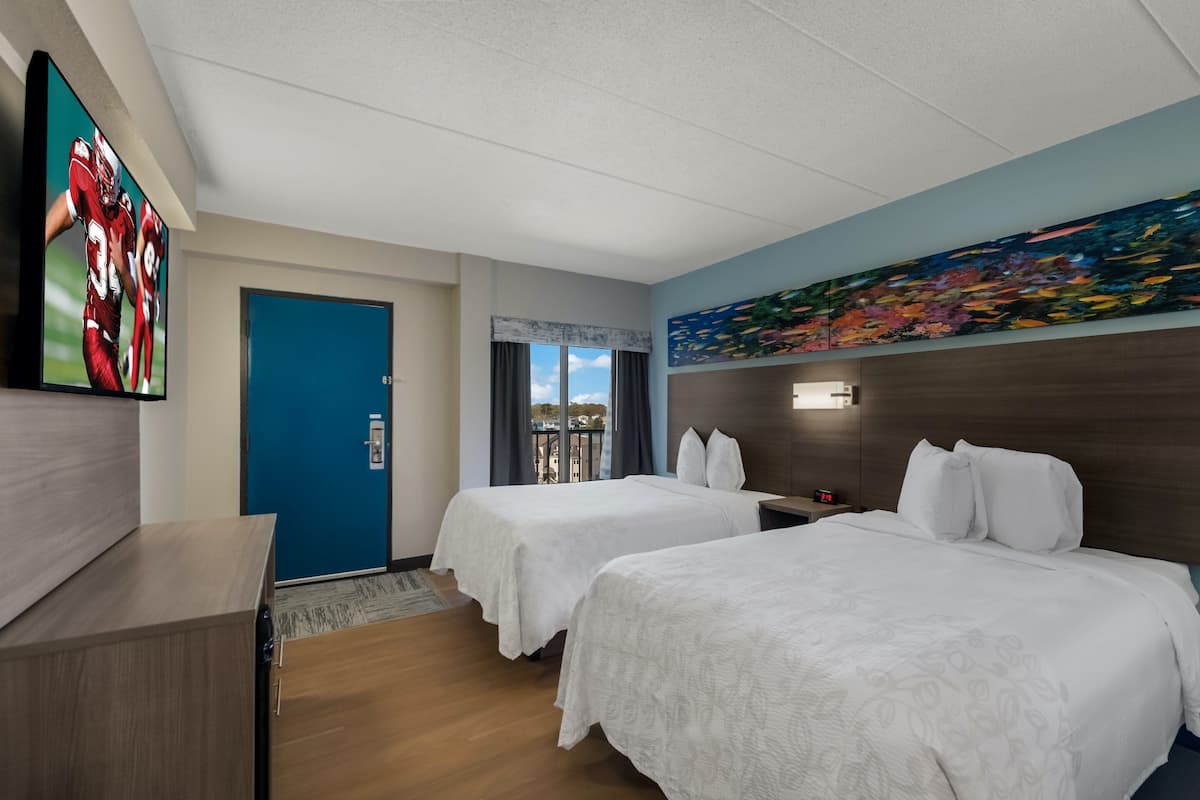 Habitación de hotel con dos camas, televisión, un cuadro y vista a la ciudad.