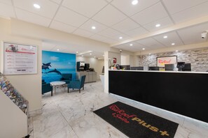A reception area with a counter, seating, a coffee machine, and a wall with a marine-themed mural. - Red Roof Inn PLUS+ & Suites Virginia Beach – Seaside (Virginia Beach)