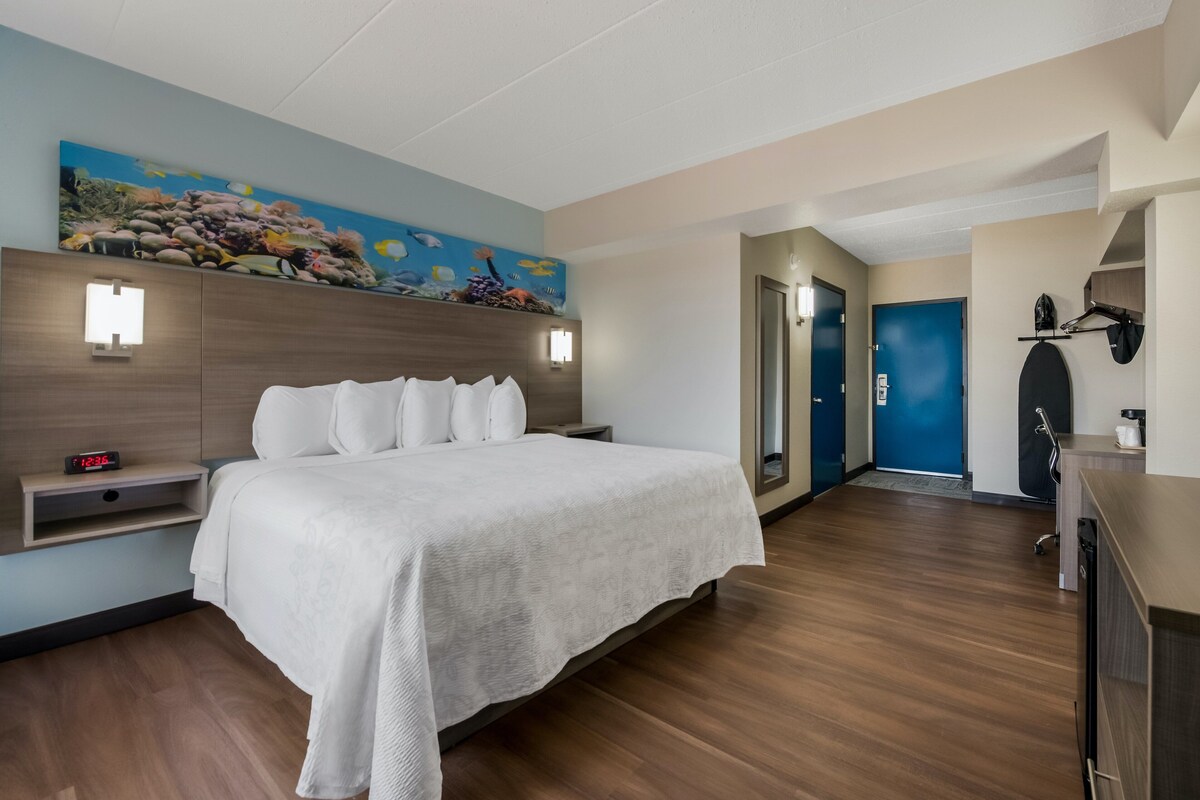 A hotel room with a bed, nightstand, wall-mounted light, and a painting of underwater scenery.
